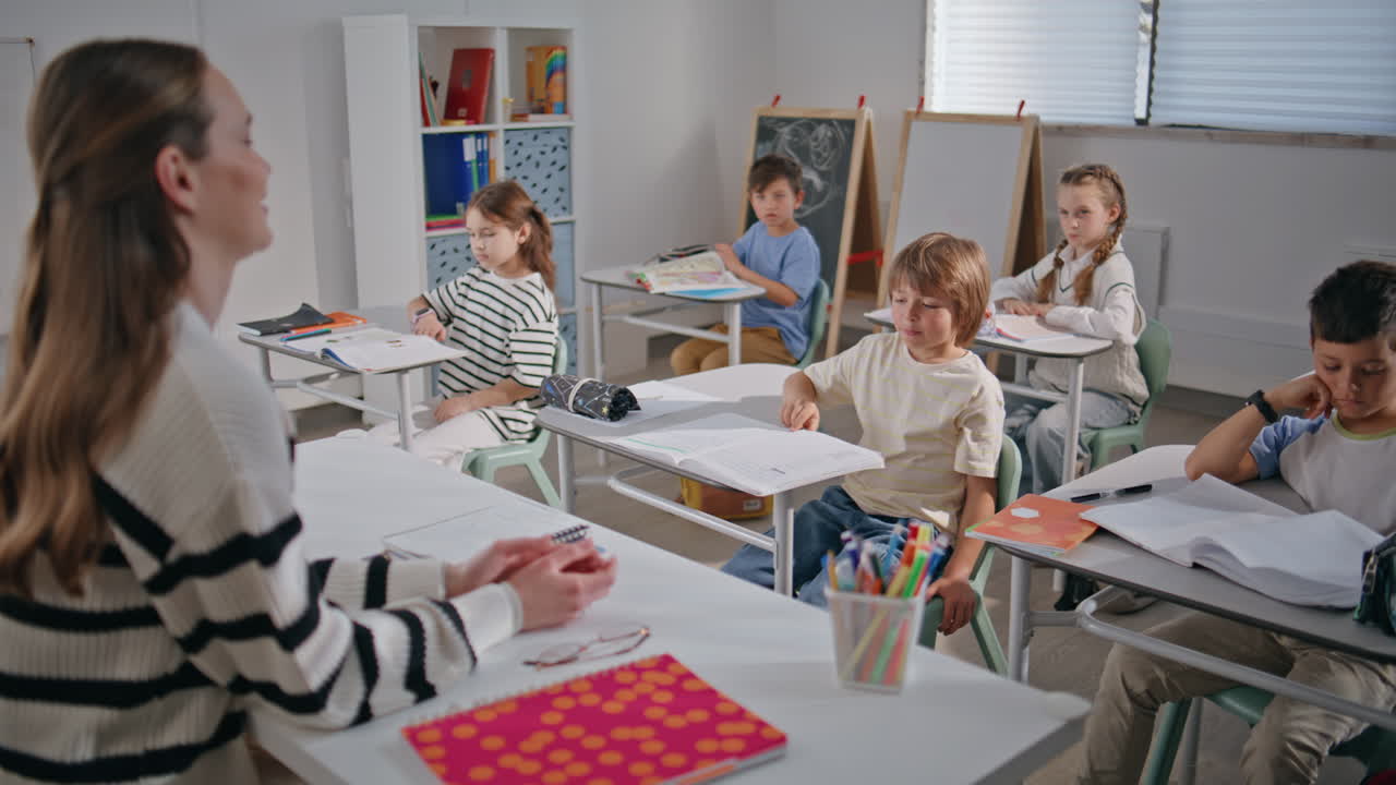Smiling teacher asking questions to kids in elementary school class room closeup