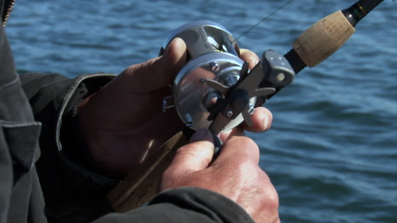 Fisherman Reeling After Catching A Fish - Man's Hand Spinning Reel With Rippling River On The Background In Woodbury, Minnesota, USA