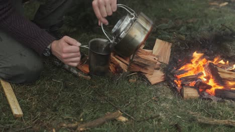 sirviendo té en una taza de cantina de una tetera de águila en el bosque junto al fuego