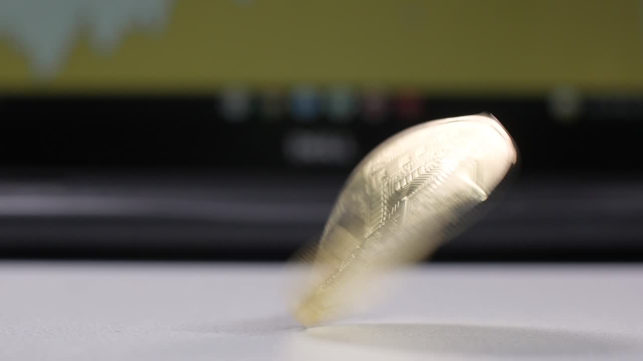 Spinning bitcoin on a white table in front of a laptop screen with a diagram