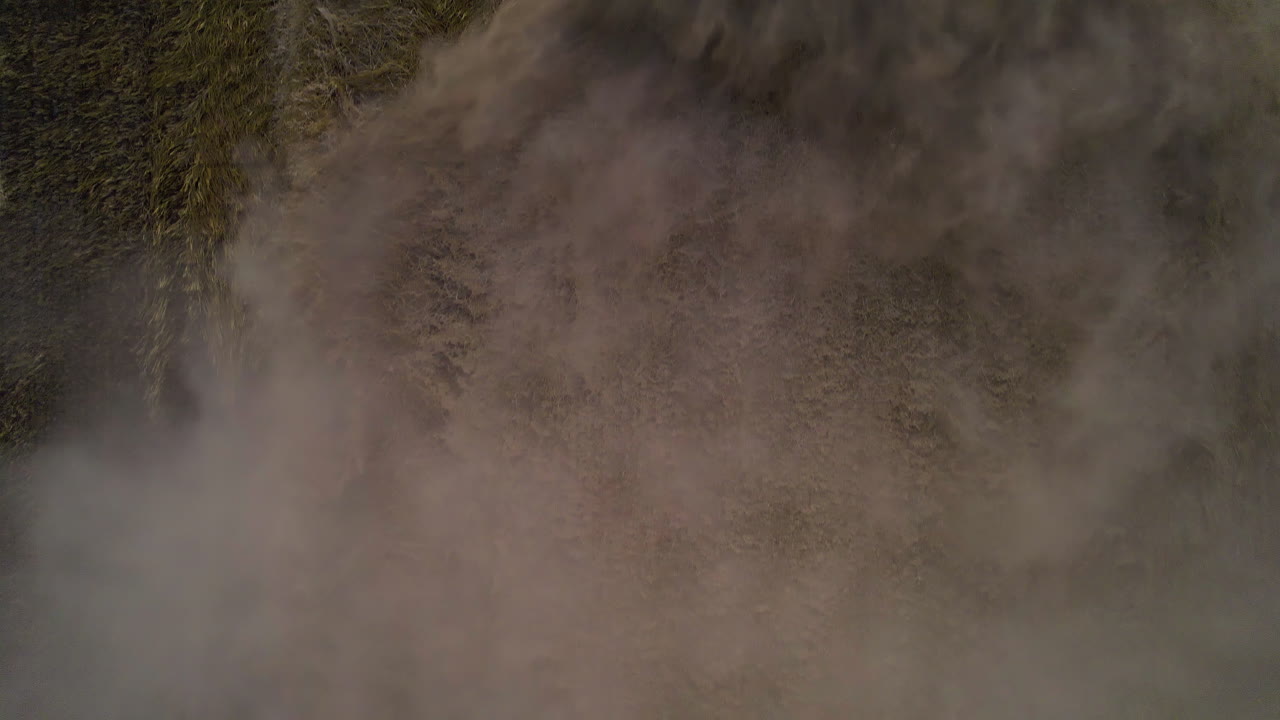 Overhead View Of Dusty Field Behind The Harvester Harvesting Crops. - aerial shot