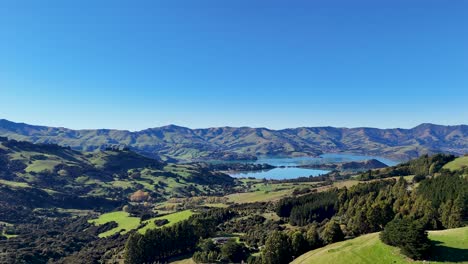 Aerial footage captures Akaroa's lush hills, serene lake, and vibrant greenery under clear blue skies