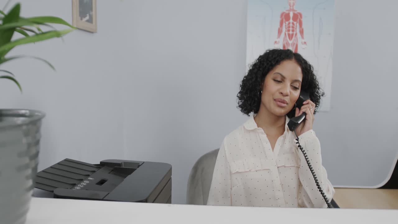 Retrato de recepcionista médica sentada na recepção, falando ao telefone, em câmera lenta