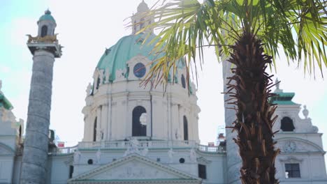 Una-Palma-Frente-A-La-Iglesia-Barroca-Blanca-Karlsplatz-Durante-El-Soleado-Día-De-Verano-En-Viena,-Austria