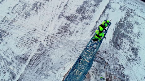 Kabelausleger-Mit-Grünen-Sicherheitsanzügen-Und-Schutzhelmen,-Die-An-Einem-Wintermorgen-Kabelreparaturen-Am-Overhead-Sendemast-Durchführen