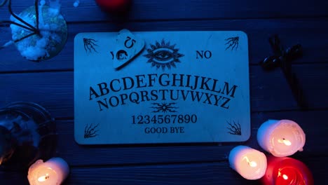 close up video of a wooden ouija board on a table surrounded by candles and a cross in a muffed - close up video of a wooden ouija board on a table. wax candles and a cross around. the planchette is slowly moving across the board, spelling out words and numbers. creative mystical content