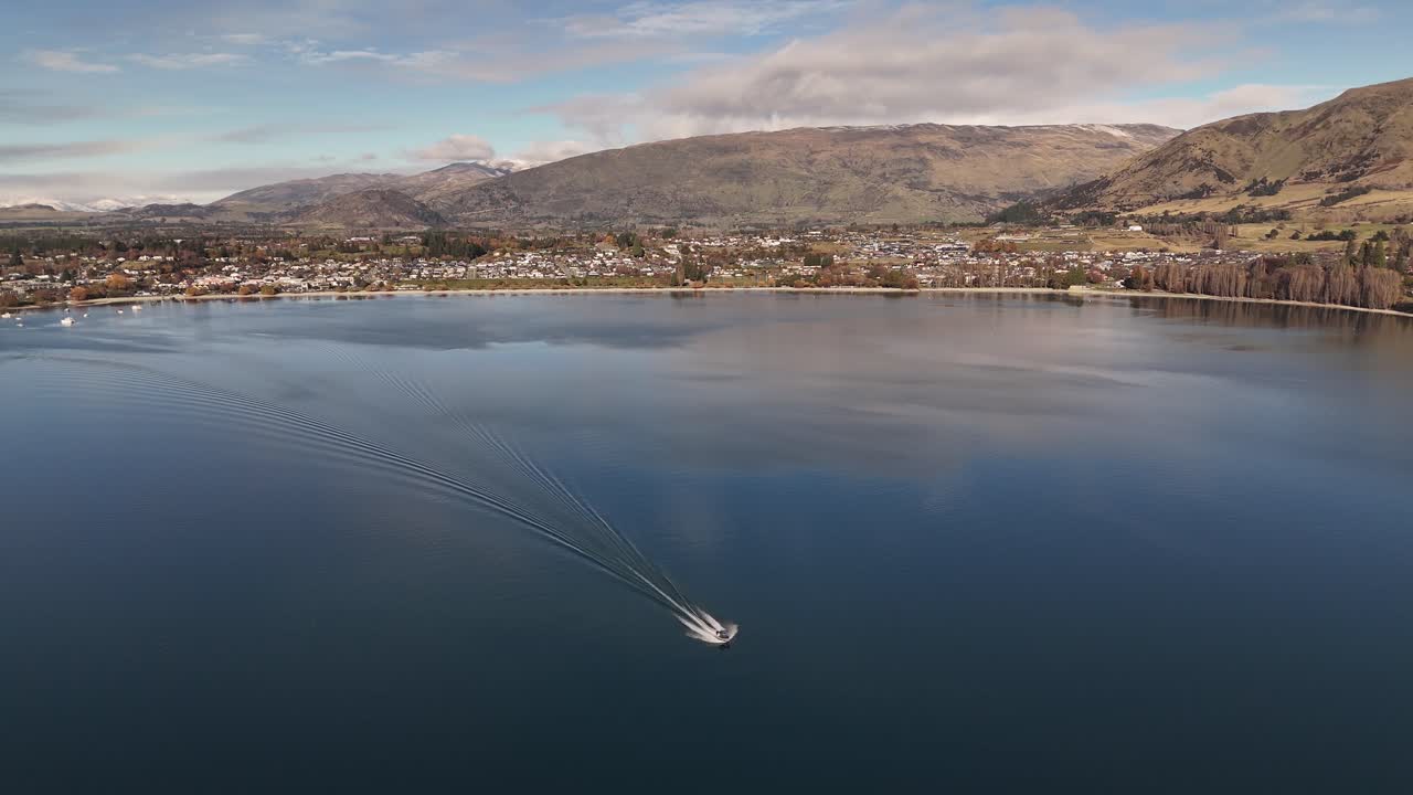 A boat sails across the flat waters of Lake Wanaka on New Zealand's South Island at sunset