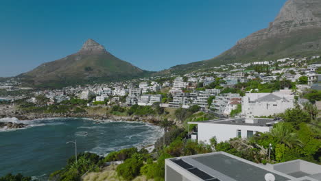 Residential-urban-borough-on-tropical-coast.-Sliding-reveal-of-waves-crashing-on-shore.-Windy-weather-on-cunny-day-with-clear-sky.-Cape-Town,-South-Africa