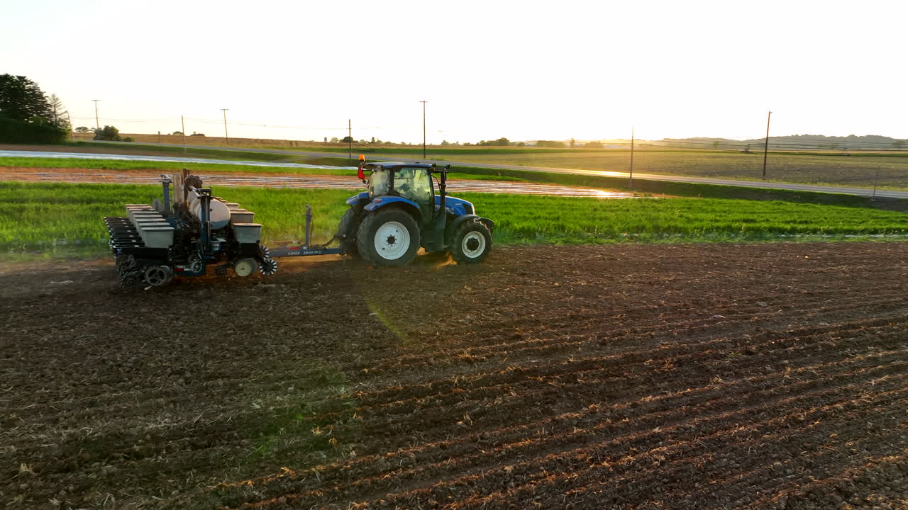 Vista de dron de un tractor tirando de una sembradora. Siembra de primavera en la América rural. La luz del sol de la hora dorada se refleja en el tractor. Rotación en el polvo de la tierra.