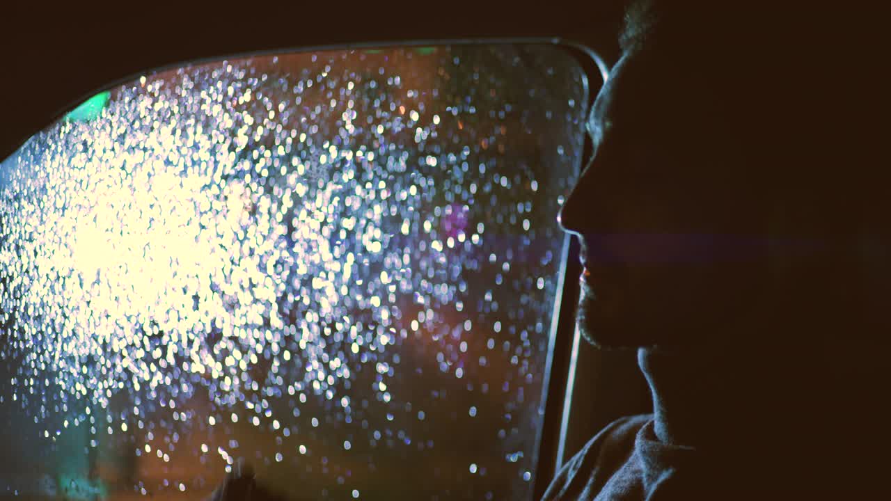 젊은 잘생긴 남자가 비가 오는 밤에 차에 앉아 있습니다.