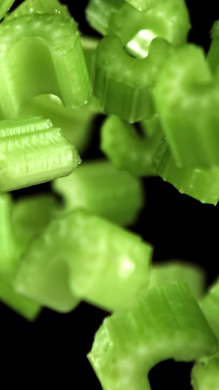 Chopped Green Celery Pieces Falling in Slow Motion on Black Background