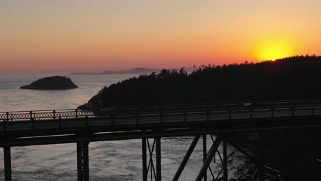 Langsame-Luftaufnahme-Eines-Autos,-Das-Durch-Den-Deception-Pass-State-Park-Fährt,-Mit-Dem-Schein-Des-Sonnenuntergangs-Im-Hintergrund