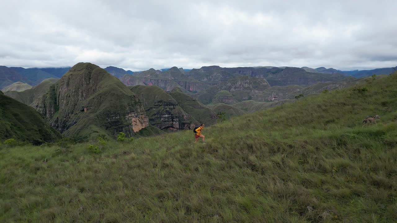 Woman hikes up ridge top trail in remote mountain range with her dog