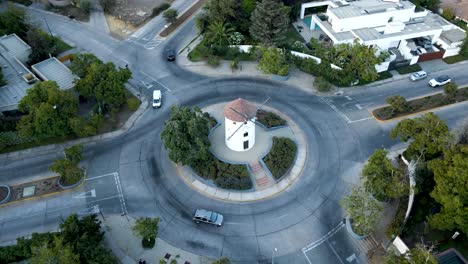 aerial orbit of leonidas montes windmill tower in roundabout with cars driving surrounded by trees, lo barnechea, santiago, chile