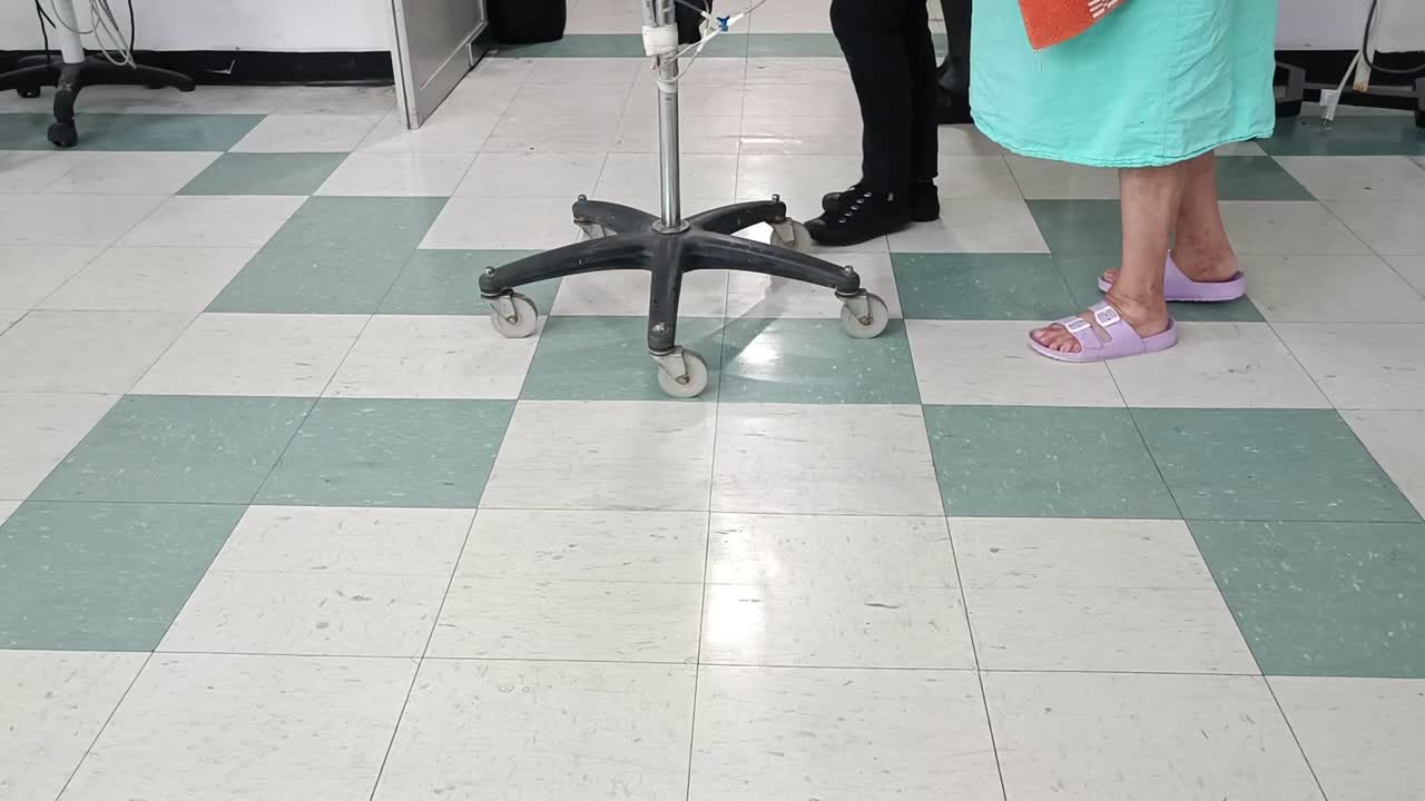 Feet of people in a tiled room with medical chairs and rolling stool visible in a clinical setting