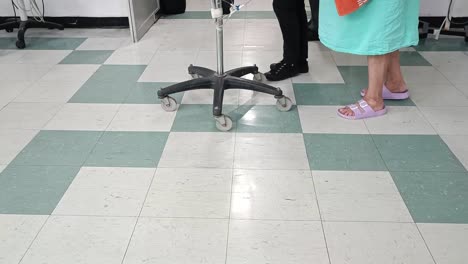 feet of people in a tiled room with medical chairs and rolling stool visible in a clinical setting