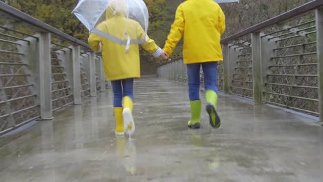 kids in rubber boots walking on bridge during rain