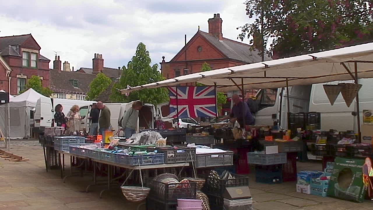 A vibrant street market scene with vendors, shoppers, and a prominent Union Jack flag.