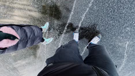 a couple skates on cracked black ice, their reflections visible on the surface
