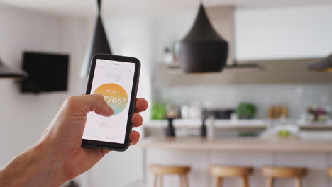 primer plano de un hombre que utiliza una aplicación en su teléfono inteligente para controlar la temperatura de la calefacción central en la casa