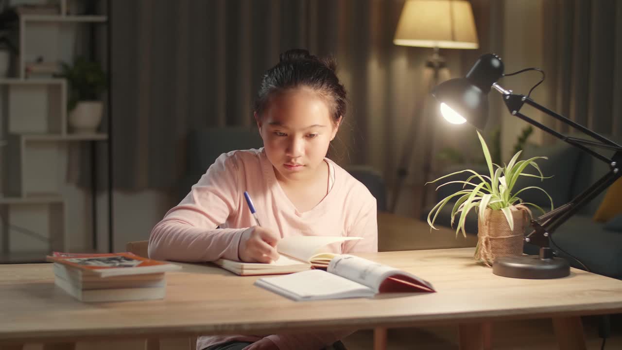 Asian Girl Is Studying At Home, Asia Child Writing While Sitting On The Table At Night