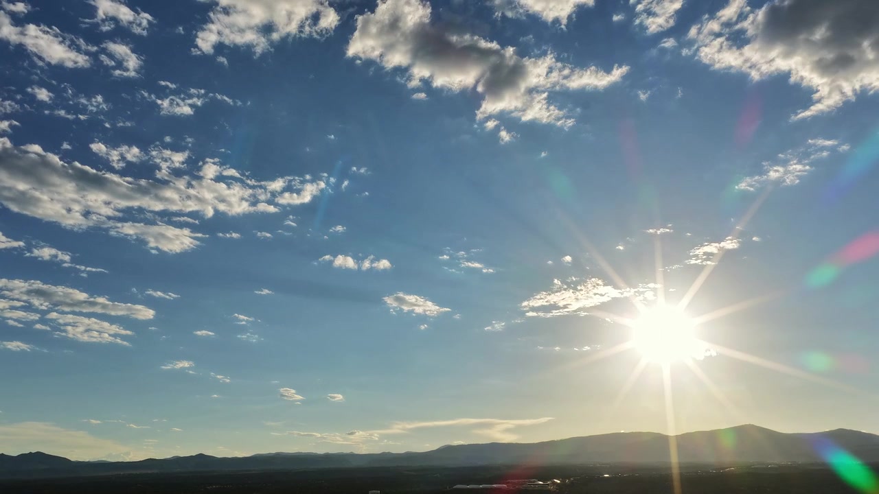 A 4k drone timelapse of the sun with brilliant lens flares and sun rays moving with clouds over a serene southwest landscape of the Jemez mountain range.
