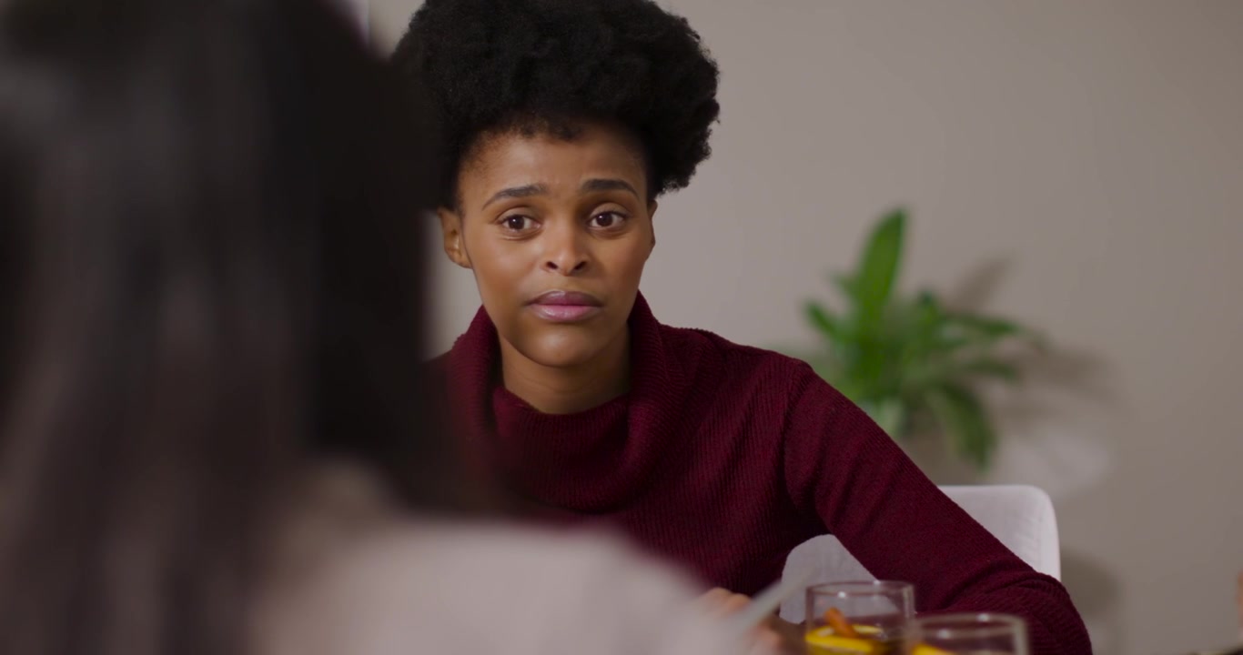 Adult African American woman raising hand and explaining after prompt at table in burgundy sweater