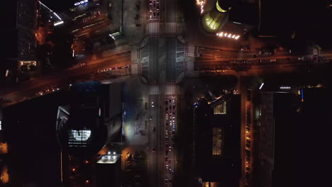 Vista-Aérea-De-Los-Pájaros-Vista-De-Arriba-Hacia-Abajo-Del-Tráfico-En-La-Ciudad-Nocturna.-Automóviles-Que-Conducen-A-Través-De-La-Intersección-Y-Otras-Direcciones-Esperando-Luz-Verde.-Varsovia,-Polonia