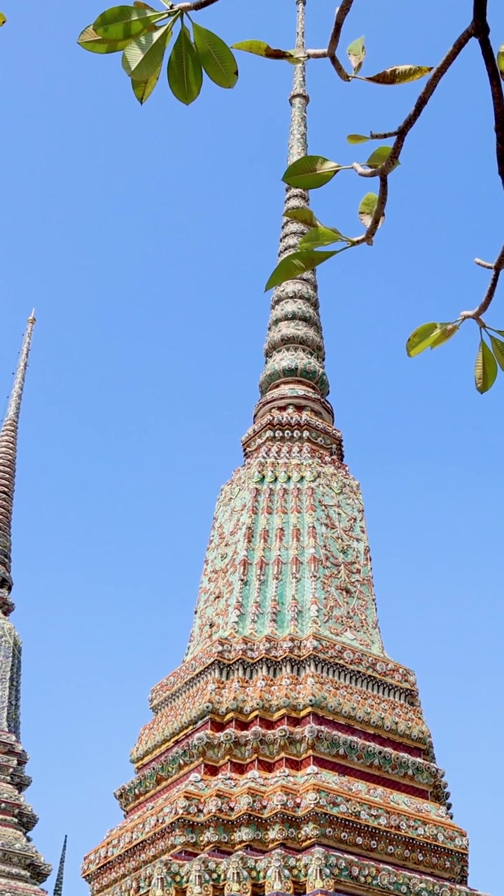 Uno scatto verticale dettagliato di una colorata guglia a pagoda a mosaico incorniciata da foglie verdi.