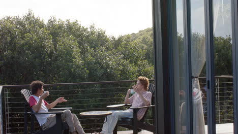 Happy-diverse-gay-male-couple-drinking-coffee-on-balcony-at-home,-slow-motion