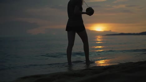 Frauen,-Die-Mit-Einer-Frischen-Kokosnuss-In-Der-Hand-Bei-Sonnenuntergang-Am-Strand-Spazieren-Gehen