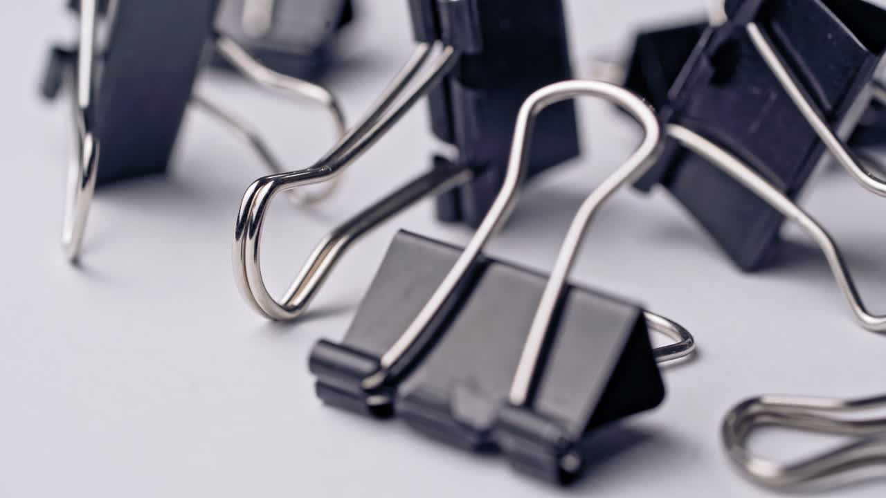 Black paper clips rotate on white background. Office supplies
