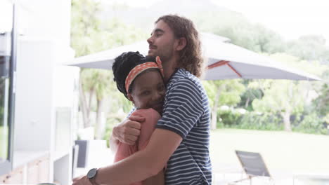 una pareja diversa, una joven afroamericana y un hombre caucásico se están abrazando en casa.