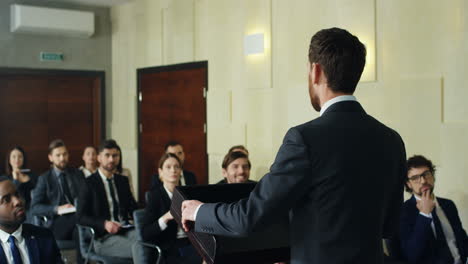 back view of caucasian male speaker standing in front of the big auditory of people at business conference