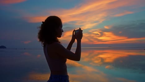 woman photographing a sunset at the beach