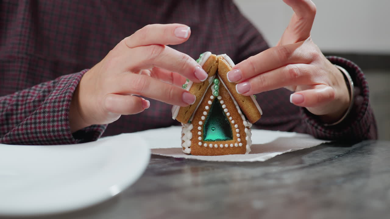 primer plano del proveedor estabilizando la galleta de casa de pan de jengibre recién montada con hielo delicado y decoraciones intrincadas, sosteniendo cuidadosamente la estructura