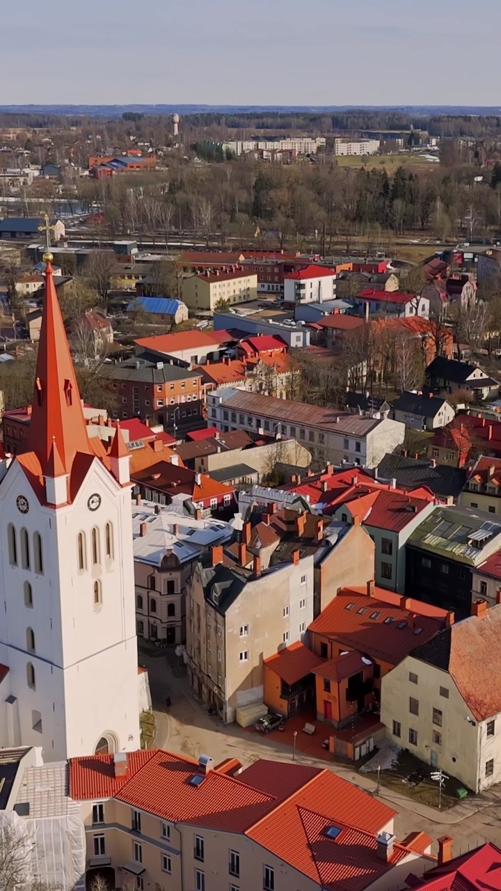Vertical aerial view of Cesis old town with a white church tower and red rooftops, capturing historic urban character in bright spring sunlight.