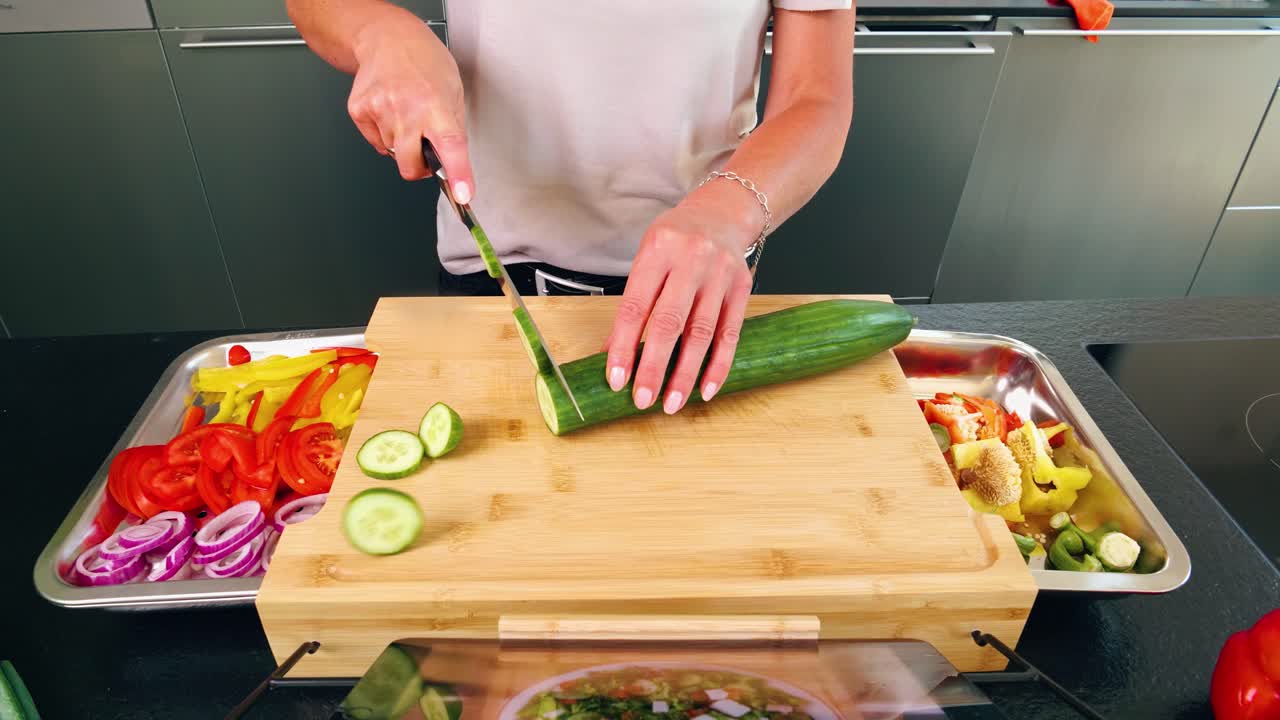 Eye perspective on a cutting board with knife and sliced cucumber with other vegetables and tablet with recipe