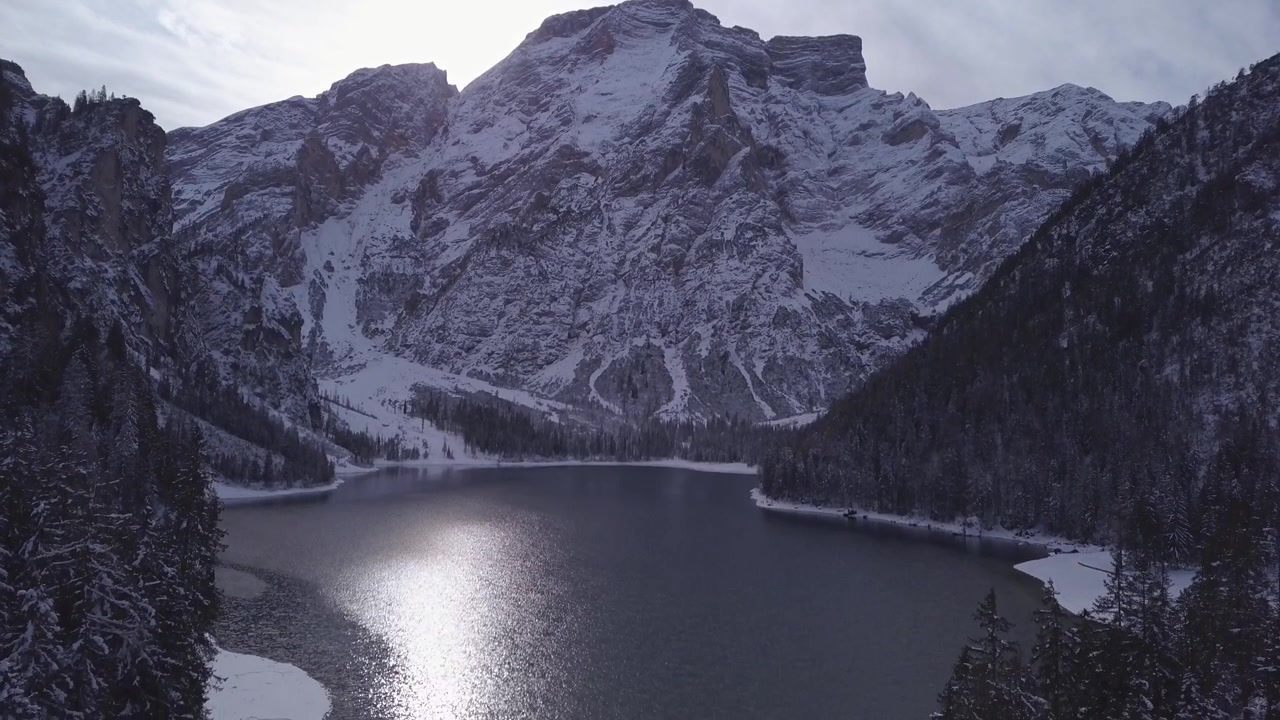 Un sereno lago alpino riflette cime innevate sotto la luce soffusa dell'alba, creando una scena tranquilla.