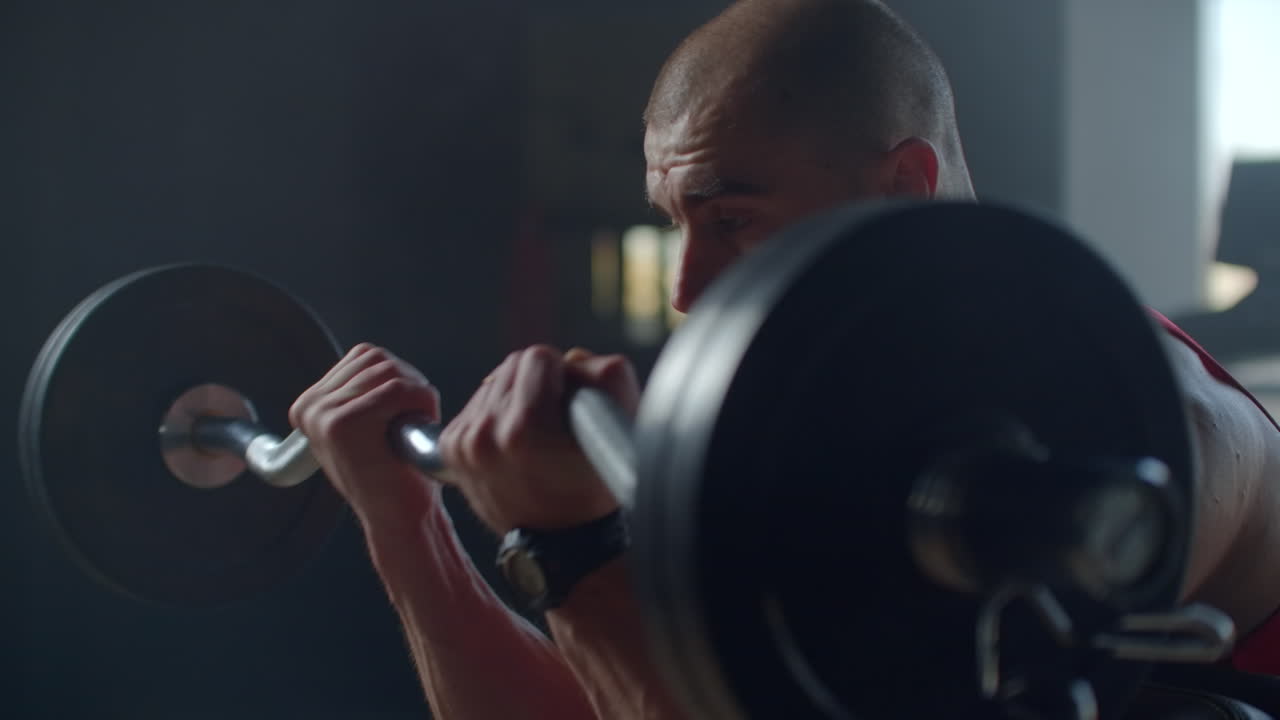 Young strong sweaty man biceps workout training with heavy barbell in the gym dark with shadows real people. Young strong muscular sweaty man with big