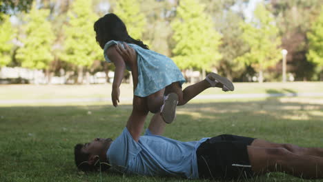 happy asian father lying on grass and raising little daughter