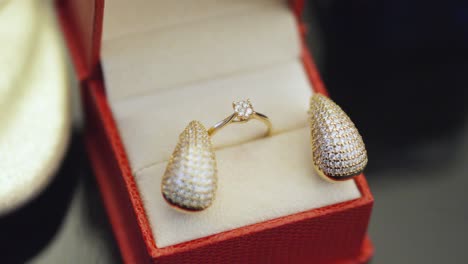 Primer-Plano-De-Aretes-De-Diamantes-Y-Anillo-De-Oro-Dentro-De-Una-Caja-Roja