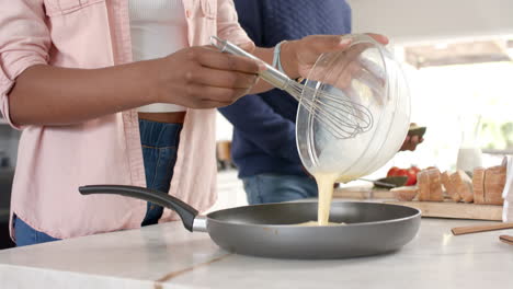 pouring batter into frying pan, african american woman cooking breakfast with partner in kitchen