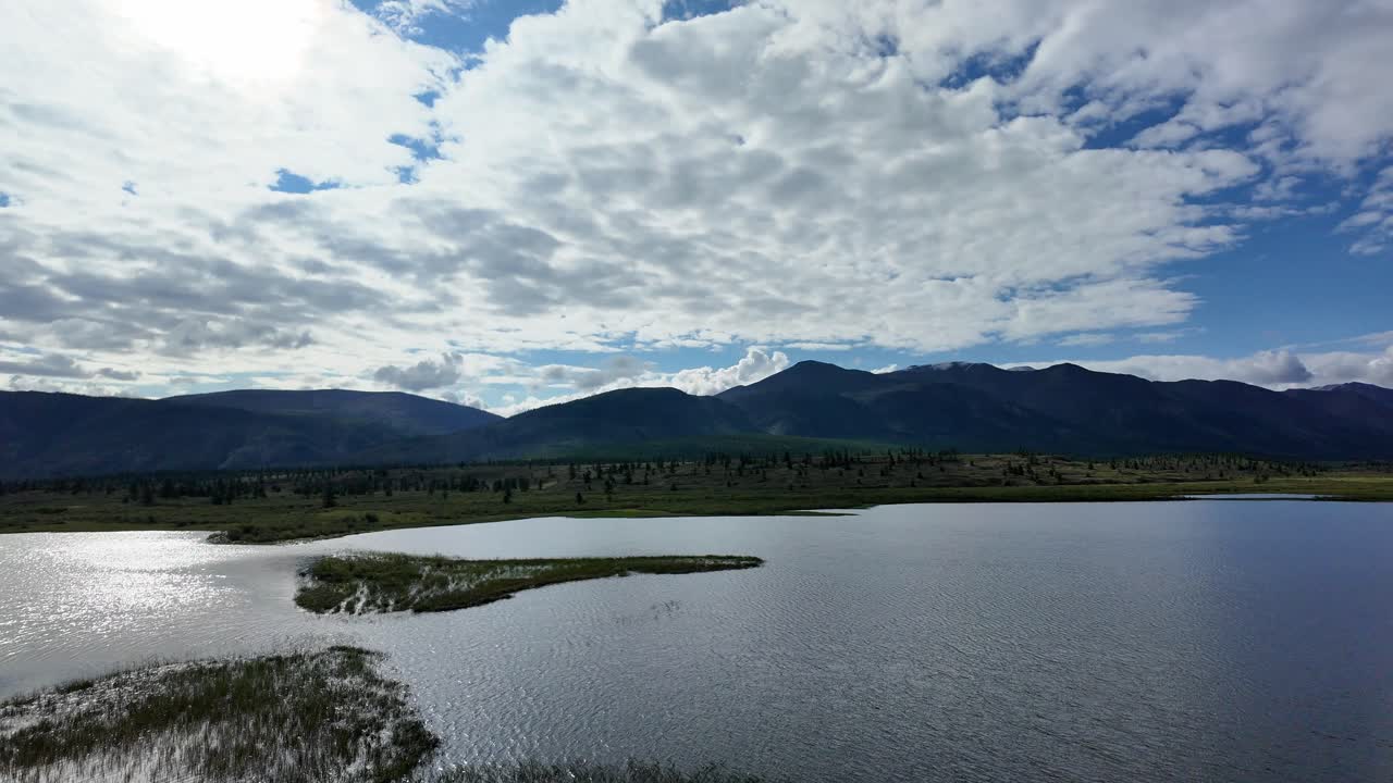 experimenta la tranquilidad de yakutia mientras majestuosas montañas se elevan sobre aguas relucientes, enmarcadas por un cielo brillante lleno de nubes dinámicas.