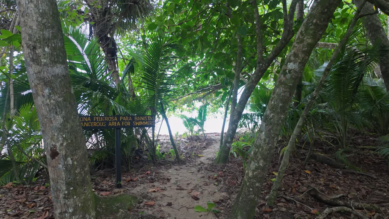 A warning sign of a dangerous area for swimmers on the path leading to the sea in Cahuita National Park, Costa Rica