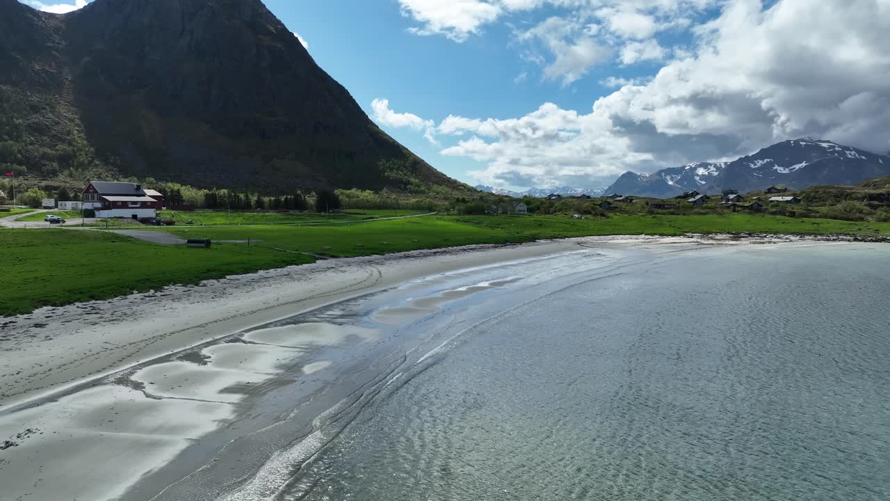 Hov beach in Gimsoy, Lofoten, with sand, waves, green meadows, farm and Hoven mountain in summer light
