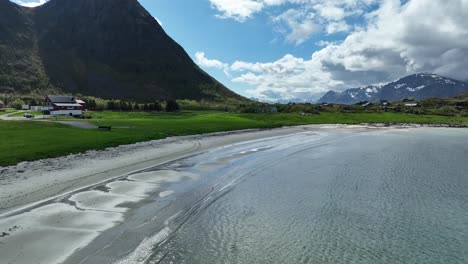 hov beach in gimsoy, lofoten, with sand, waves, green meadows, farm and hoven mountain in summer light