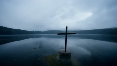 clouds pass over a tranquil lake, revealing a cross emerging from the water during the serene early morning hours