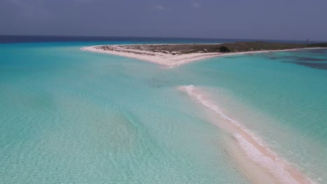 Aerial-pullback-above-sand-island-with-crystal-clear-light-blue-ocean-water-waves