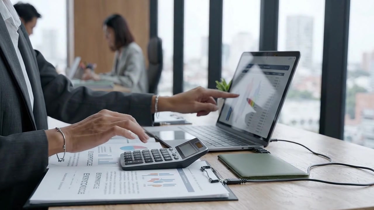 Una scena d'ufficio professionale che mostra individui concentrati impegnati nell'analisi finanziaria, utilizzando laptop e calcolatrici, all'interno di un ambiente di lavoro moderno con vista sulla città